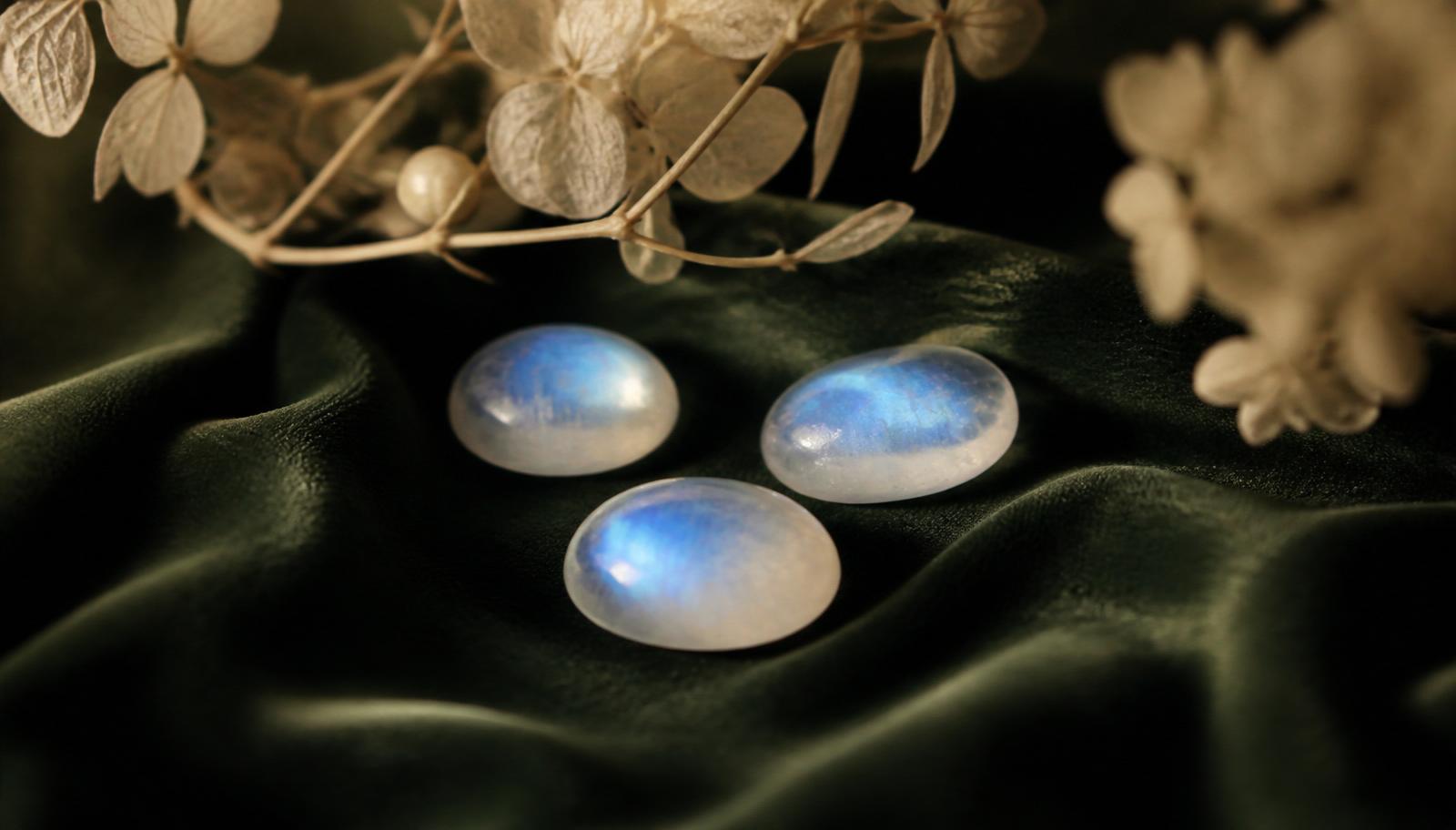 Twee maansteen-cabochons met zachte blauwe schiller op flessengroen fluweel — sfeerbeeld, geen determinatievoorbeeld.